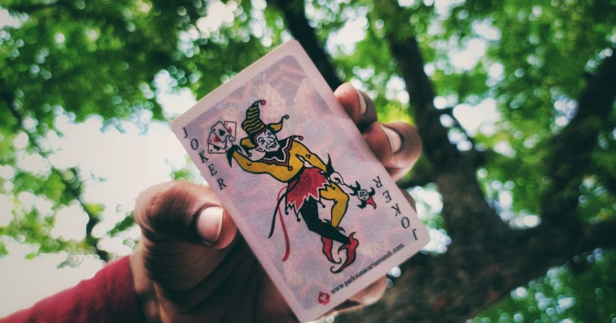 深色桌面上一副摊开的扑克牌，纸牌接龙的七列牌堆整齐排列，暖色台灯从侧面打光，屏幕里映出牌面与紫色光晕，整体是安静专注的深夜研究氛围